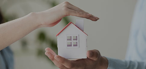 ceci est la photo de deux personnes, une tient dans sa main une maison miniature, l'autre la recouvre d'une main comme pour faire un abrit